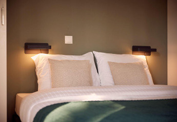 Modern tweepersoonsbed met witte kussens en gezellige verlichting in Holiday villa Amalia 6, Hofparken De Bergvennen, Nederland.