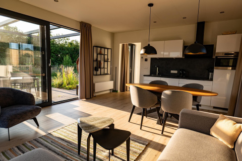 Sala luminosa y moderna en una cabaña con grandes ventanales, cocina abierta y vistas al jardín exterior.
