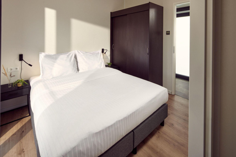 Modernes Lodge-Schlafzimmer mit Doppelbett, weißen Bettlaken, Schrank und Nachttischen mit Pflanzen.