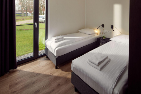 Habitación de cabaña moderna con dos camas individuales, grandes ventanales y vista a césped verde afuera.