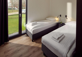 Moderne lodge kamer met twee eenpersoonsbedden, grote ramen en uitzicht op groen gazon buiten.
