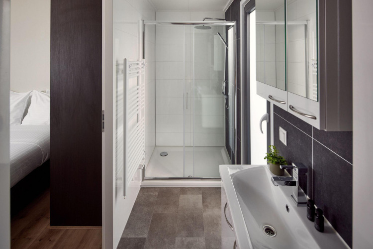 Modernes Badezimmer in einer Lodge mit Glasdusche, großem Spiegel, Waschbecken und angrenzendem Schlafzimmer.