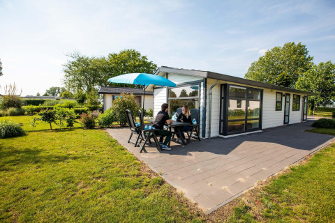 Deux personnes assises à la terrasse d’un chalet Comfort à EuroParcs Noordwijkse Duinen aux Pays-Bas.