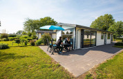 To personer sidder udenfor på terrassen ved en Comfort-hytte på EuroParcs Noordwijkse Duinen i Holland.