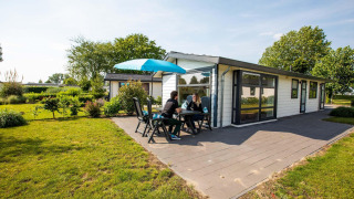 Deux personnes assises à la terrasse d’un chalet Comfort à EuroParcs Noordwijkse Duinen aux Pays-Bas.