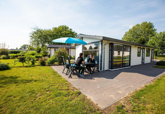 Deux personnes assises à la terrasse d’un chalet Comfort à EuroParcs Noordwijkse Duinen aux Pays-Bas.