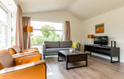 Lichte, moderne woonkamer in een Comfort-hut bij EuroParcs Noordwijkse Duinen met grote ramen en stijlvolle inrichting.