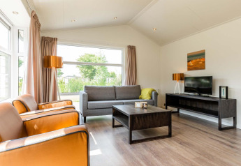 Heldere, moderne woonkamer in een Comfort-cabine bij EuroParcs Noordwijkse Duinen met grote ramen en stijlvolle inrichting.