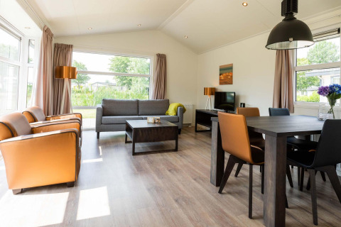 Sala de estar luminosa y moderna en la cabaña Comfort de EuroParcs Noordwijkse Duinen, Países Bajos, con grandes ventanales.