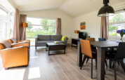 Salon moderne et lumineux dans le chalet Comfort d’EuroParcs Noordwijkse Duinen, Pays-Bas, avec de grandes fenêtres.