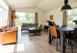 Luminoso e moderno soggiorno nella cabina Comfort di EuroParcs Noordwijkse Duinen, Paesi Bassi, con ampie finestre.