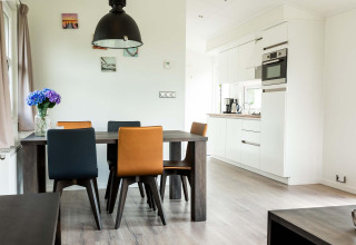 Salle à manger moderne avec chaises colorées et cuisine dans un chalet à EuroParcs Noordwijkse Duinen, Pays-Bas.