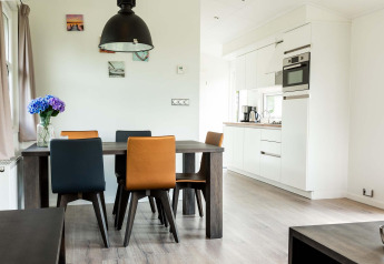 Moderne eethoek met gekleurde stoelen en keuken in een huisje bij EuroParcs Noordwijkse Duinen, Nederland.