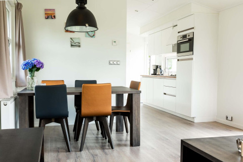 Moderne eethoek met kleurrijke stoelen en keuken in een chalet bij EuroParcs Noordwijkse Duinen, Nederland.