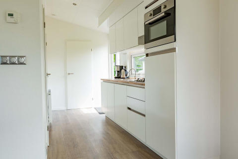 Moderne, lichte cabinakeuken met witte kasten, inbouwapparatuur en houten vloer bij EuroParcs Noordwijkse Duinen.
