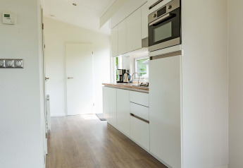 Moderne, lichte cabinakeuken met witte kasten, inbouwapparatuur en houten vloer bij EuroParcs Noordwijkse Duinen.