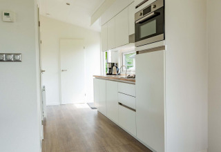 Moderne, heldere keuken in een cabin met witte kasten, ingebouwde toestellen en houten vloer bij EuroParcs Noordwijkse Duinen.