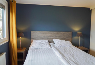 Dormitorio moderno en una cabaña Comfort de EuroParcs Noordwijkse Duinen con cama doble, lámparas y pared azul.