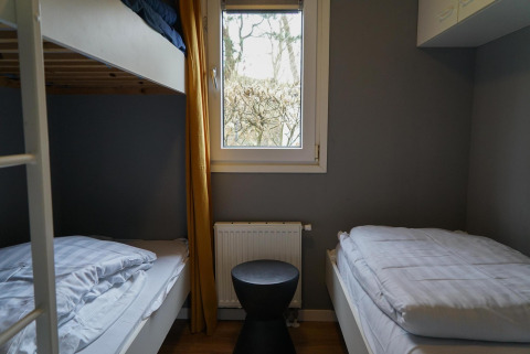 Chambre confortable dans une cabine avec lit superposé et lit simple à EuroParcs Noordwijkse Duinen.