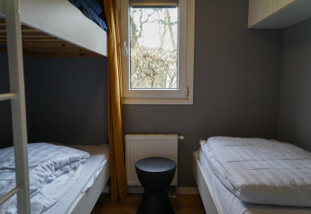 Chambre confortable dans une cabine avec lit superposé et lit simple à EuroParcs Noordwijkse Duinen.