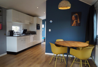 Moderne keuken en eetgedeelte met gele stoelen in Comfort cabin bij EuroParcs Noordwijkse Duinen, Nederland.