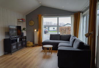 Salon d’un chalet moderne à EuroParcs Noordwijkse Duinen avec canapé gris et grandes baies vitrées.