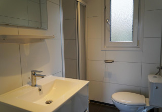 Bagno con lavandino, specchio, WC e finestra in una cabina Comfort a EuroParcs Noordwijkse Duinen, Paesi Bassi.