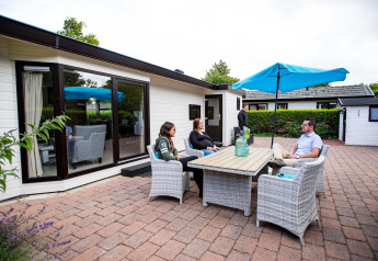 Vier mensen ontspannen aan een buitentafel voor een vakantiehuis bij EuroParcs Noordwijkse Duinen.