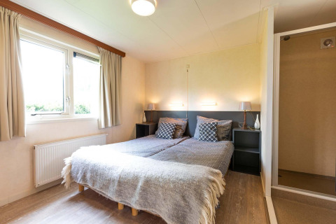 Camera nella casa vacanze di EuroParcs Noordwijkse Duinen con due letti singoli e ampia finestra luminosa.