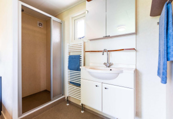 Salle de bain moderne avec douche, lavabo et serviettes bleues dans un chalet à EuroParcs Noordwijkse Duinen, Pays-Bas.