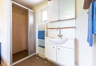 Salle de bain moderne avec douche, lavabo et serviettes bleues dans un chalet à EuroParcs Noordwijkse Duinen, Pays-Bas.