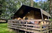 Tienda safari llamada Summer Lodge con terraza de madera en Beerze Bulten, Países Bajos, rodeada de árboles.