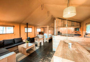 Interior de la tienda safari Summer Lodge en Beerze Bulten, Países Bajos, con muebles de madera y luz natural.