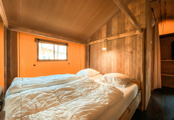 Acogedor dormitorio en una tienda safari llamada Summer Lodge en Beerze Bulten, Países Bajos, con paredes de madera.