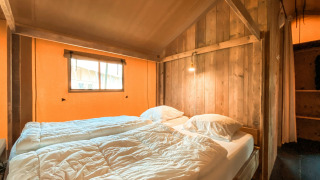 Acogedor dormitorio en una tienda safari llamada Summer Lodge en Beerze Bulten, Países Bajos, con paredes de madera.
