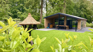 Lodge familial moderne avec terrasse et jardin verdoyant à De Thijmse Berg, Pays-Bas, entouré d'arbres.