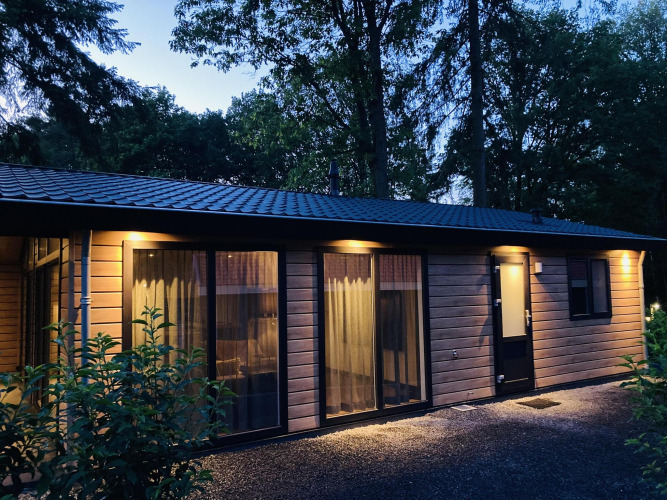 Photo du soir de la Family Lodge Deluxe à De Thijmse Berg aux Pays-Bas avec fenêtres éclairées et arbres.