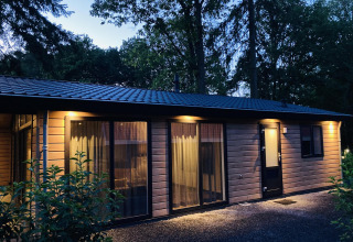 Abendaufnahme der Family Lodge Deluxe bei De Thijmse Berg in den Niederlanden mit beleuchteten Fenstern.