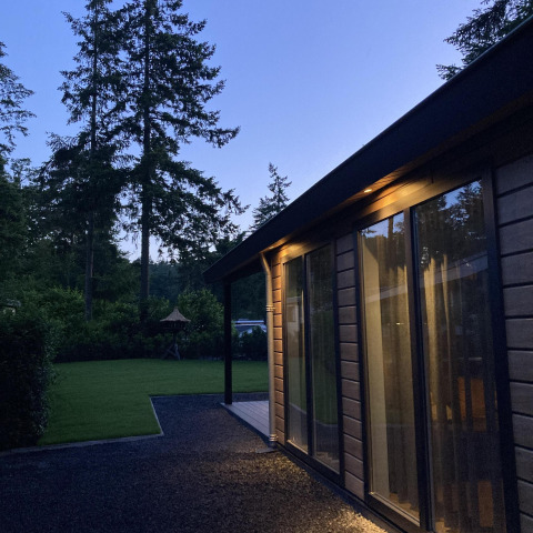 Vista nocturna de la Family Lodge Deluxe en De Thijmse Berg, Países Bajos, rodeada de árboles y césped.