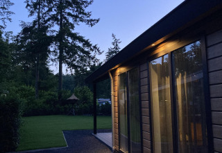 Abendaufnahme der Family Lodge Deluxe bei De Thijmse Berg, Niederlande, umgeben von Wald und Rasenflächen.