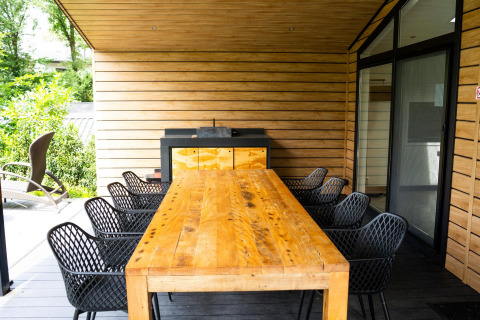 Comedor exterior con mesa de madera y sillas negras en Family Lodge Deluxe, De Thijmse Berg, Países Bajos.