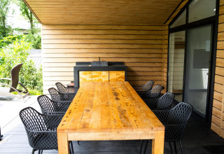 Comedor exterior con mesa de madera y sillas negras en Family Lodge Deluxe, De Thijmse Berg, Países Bajos.