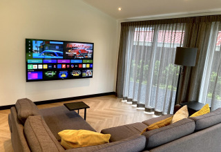 Sala moderna en Family Lodge Deluxe en De Thijmse Berg, Países Bajos, con sofá, televisor y grandes ventanales.