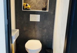 Moderne toilet i Family Lodge Deluxe på De Thijmse Berg, Nederlandene, med mørke vægge og nichedekor.