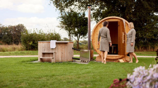 Due persone in accappatoio si godono una sauna a botte e una vasca all’aperto nel giardino di un lodge.