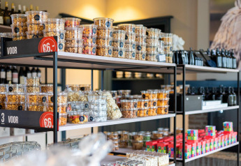 Billede af en butikshylde i en lodge med forskellige nødder og snacks i plastbeholdere til salg.