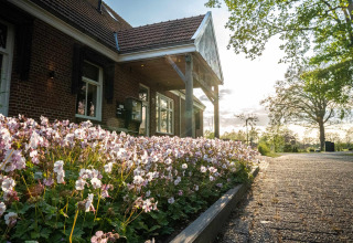 Photo d’un lodge avec un parterre de fleurs roses devant, allée pavée et arbres au coucher du soleil.