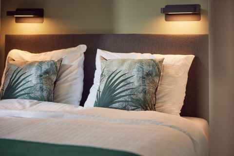 Cama moderna con cojines de hojas y luces de pared en Water lodge 6 Deluxe, Hofparken Wiltershaar, Países Bajos.
