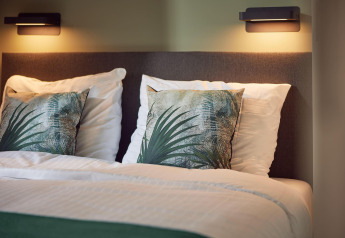 Moderne seng med to puder og plantemotiver, oplyst af væglamper på Water lodge 6 Deluxe i Holland.