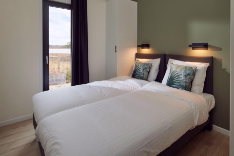 Dormitorio con dos camas individuales, ropa de cama blanca y vista a la naturaleza en Water lodge 6 Deluxe en Hofparken Wiltershaar.